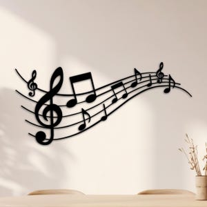 Puede incluir: Arte mural de metal negro con notas musicales y símbolos, incluyendo una clave de sol y corcheas, dispuestas sobre un pentagrama ondulado. La pieza decorativa está diseñada para montarse en la pared, añadiendo un tema musical a cualquier habitación.
