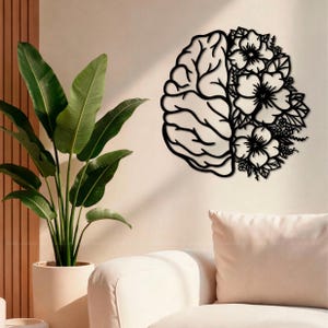 May include: A black wall art piece featuring a split design where one half depicts the anatomical structure of a human brain and the other half consists of detailed floral patterns with various blossoms and leaves in a cohesive silhouette.