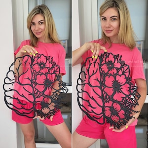 May include: A black laser-cut wall art piece featuring a split design where one side depicts the anatomical structure of a human brain and the other side displays a detailed arrangement of blooming flowers and leaves with intricate cutouts.