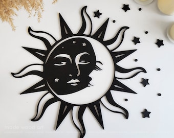 Puede incluir: Decoración de pared de madera en blanco y negro con un sol y una luna con cara. El sol tiene rayos y la luna es una media luna. Hay pequeñas estrellas dispersas alrededor del sol y la luna.