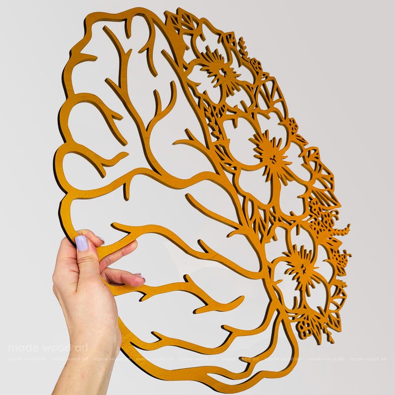 May include: A mustard yellow laser-cut wooden wall art piece shaped like a human brain. The left side features branching, root-like lines, while the right side is filled with intricate, detailed floral patterns and blossoms throughout the structure.