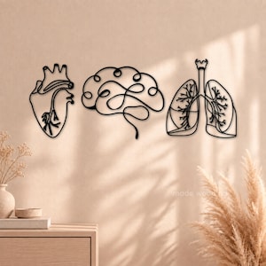 May include: Three black metal wall art pieces featuring continuous line drawings of human anatomy. The set includes a stylized heart, a brain with intricate looping lines, and a pair of lungs with detailed bronchial structures, all in black.