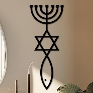 May include: Black wooden wall art featuring a menorah, Star of David, and fish symbol. The artwork is mounted on a neutral-colored wall, with a minimalist design. The piece is a decorative item for home decor.