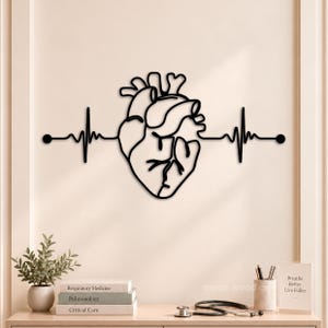 May include: A black wall-mounted metal art piece featuring a continuous line drawing of an anatomical human heart integrated with a horizontal heartbeat rhythm line, ending in two circular dots on either side of the central heart design.