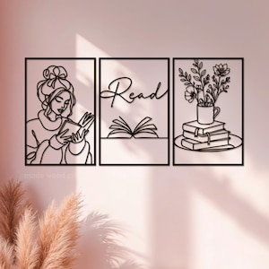 May include: Three-panel wall art set with a reading theme. The panels feature laser-cut designs of a woman reading, the word "Read" above an open book, and flowers in a mug atop books. The art is in a minimalist style with a black finish.