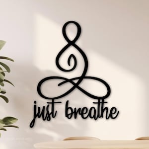 May include: Black wooden wall art featuring a stylized figure in a seated yoga pose with the words "just breathe" in a cursive font. The art piece is mounted on a light-colored wall, suggesting a minimalist or zen-inspired decor.