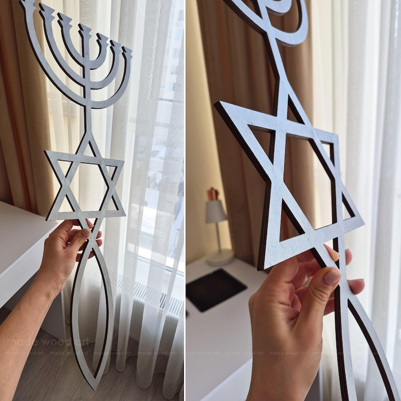May include: Wooden wall art featuring a Menorah, Star of David, and a fish symbol. The art piece is made of dark brown wood with a light gray interior. The Menorah has nine candle holders. The Star of David is a six-pointed star.