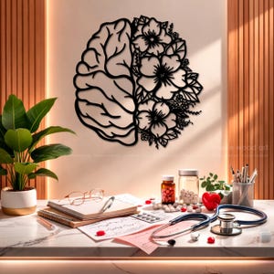 May include: A black wall art piece featuring a split design with a human brain on the left side and a cluster of blooming flowers and leaves on the right side. The piece is mounted on a light-colored wall above a desk with medical supplies.