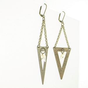 May include: A pair of bronze-toned earrings. Each earring features a triangular pendant with a chain and a small, white, tooth-shaped charm. The earrings have a lever-back closure.
