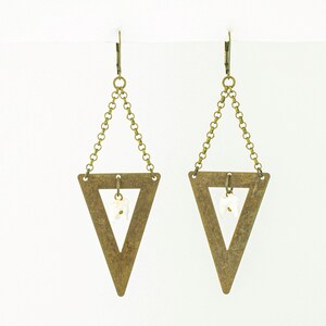 May include: A pair of brass-toned triangle earrings. Each earring features a large, open triangle pendant suspended from a chain and a small, white, irregular-shaped stone. The earrings have a simple, geometric design.