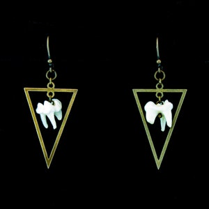 Puede incluir: Un par de pendientes triangulares de oro con un dije de diente blanco colgando de cada uno.