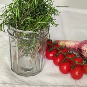 Peut inclure: Un bocal en verre rempli de brins de romarin frais, une gousse d'ail violette et une grappe de tomates cerises rouges.