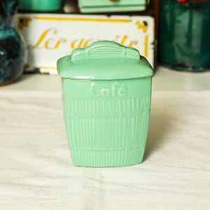 Op de afbeelding: Een vintage groene keramische koffiebus met een deksel en het woord "Cafe" op de voorkant.