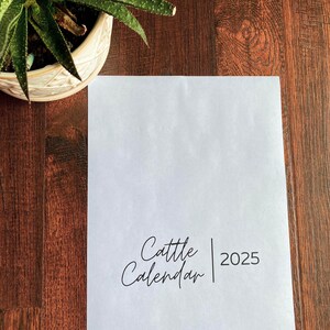 Könnte beinhalten: Ein weißes Blatt Papier mit dem Text "Cattle Calendar | 2025" in schwarzer Tinte gedruckt.