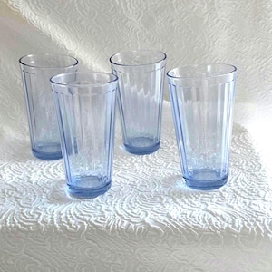 May include: A set of four light blue drinking glasses, each featuring a vertical ribbed pattern along the exterior walls. The glasses have a tapered cylindrical shape with a smooth rim and a slightly thicker base, providing a consistent look.