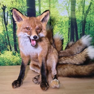 May include: A detailed, lifelike fox sculpture with multiple fluffy tails. The fox has reddish-brown fur, a white chest, and black legs. Its mouth is open, revealing its teeth. The background features a forest scene.