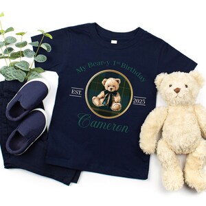 May include: Navy blue t-shirt with a teddy bear graphic and the text "My Bear-y 1st Birthday Cameron 2025". Includes navy pants, blue slip-on shoes, and a stuffed teddy bear. A perfect gift for a child's birthday.