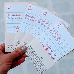 Puede incluir: Cuatro marcadores de estilo tarjeta de biblioteca blancos con l&iacute;neas azules y texto rojo. El texto en los marcadores dice "FIC BRO" y "Bront&euml;, Emily Wuthering Heights". El texto "Whatever our souls are made" est&aacute; escrito en rojo en el marcador inferior.