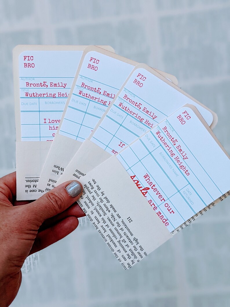 Puede incluir: Cuatro marcadores de estilo tarjeta de biblioteca blancos con l&iacute;neas azules y texto rojo. El texto en los marcadores dice "FIC BRO" y "Bront&euml;, Emily Wuthering Heights". El texto "Whatever our souls are made" est&aacute; escrito en rojo en el marcador inferior.