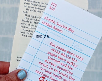 Op de afbeelding: Een blauwe bibliotheekkaart met witte lijnen en rode tekst. De tekst luidt "FIC ALC", "Alcott, Louisa May", "Little Women", "DUE DATE", "DEC 25", "BORROWERS NAME", "DATE RETURNED", "The rooms were very still while the pages were softly turned and the winter sunshine crept in to touch the bright heads and serious faces with a Christmas greeting."