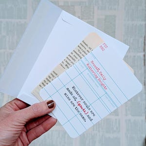 May include: A white envelope holds a card with a library card design. The card features the quote "Whatever souls are made of, (yours) and mine are the same." in red and black text. The card is a literary-themed item.