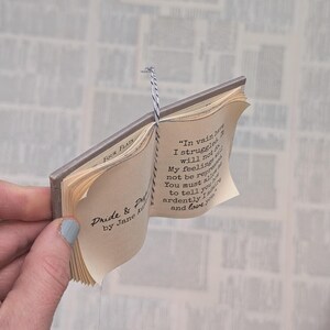 May include: A miniature book titled Pride & Prejudice by Jane Austen with a grey cover and black and white twine binding. The open pages display the text: In vain have I struggled. It will not do. My feelings will not be repressed.