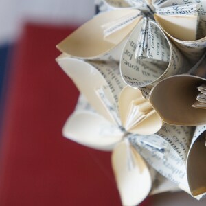 May include: A close-up of a paper flower made from the pages of a book. The flower is white and has a delicate, intricate design. The pages of the book are visible in the petals of the flower.