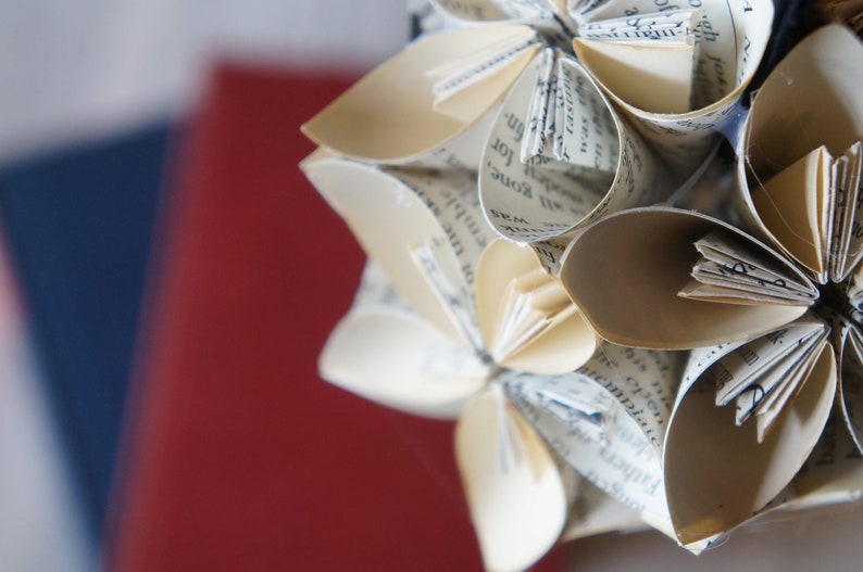 May include: A close-up of a paper flower made from the pages of a book. The flower is white and has a delicate, intricate design. The pages of the book are visible in the petals of the flower.
