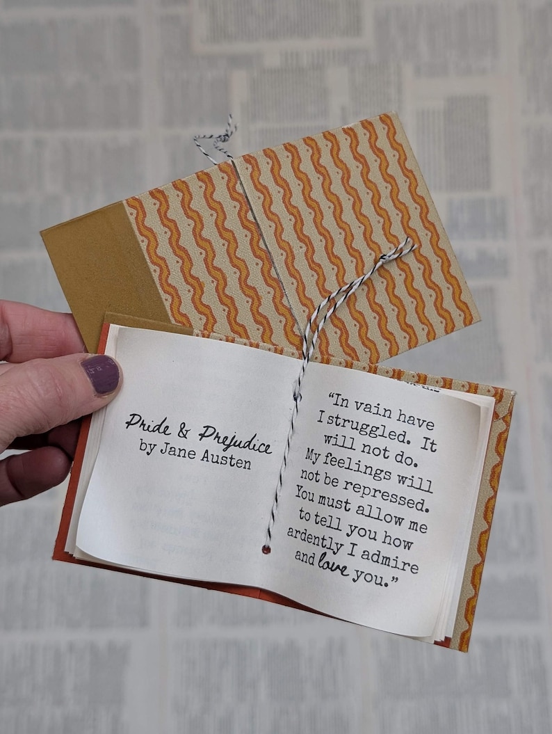 May include: A miniature book titled Pride & Prejudice by Jane Austen with a patterned orange and white wavy cover. The open pages display the text: In vain have I struggled. It will not do. My feelings will not be repressed. You must allow me to tell you how ardently I admire and love you. The book is bound with black and white twine.