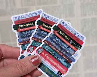 May include: Three stackable stickers featuring a stack of books with Christmas-themed titles. The stickers are white with a blue and red color scheme. The titles include "A Christmas Carol", "Christmas with Anne", "Emmanuel", "The Best Christmas Stories Ever", "Dickens of Christmas", "Charles Dickens", "Shadow & Light", "A Child's Christmas in Wales", "Christmas Album", "A Christmas Treasury", "Twas The Night Before Christmas", "By Words on a Snowy Evening", and "The Real Book Snowman".