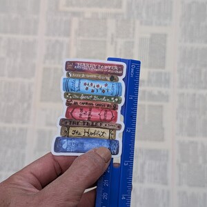 May include: A stack of book stickers featuring popular titles like "Harry Potter and the Prisoner of Azkaban", "Anne of Green Gables", "Little Women", "The Secret Garden", "Pride and Prejudice", "The Thief", and "The Hobbit". The stickers are arranged in a stack and are approximately 3 inches tall.