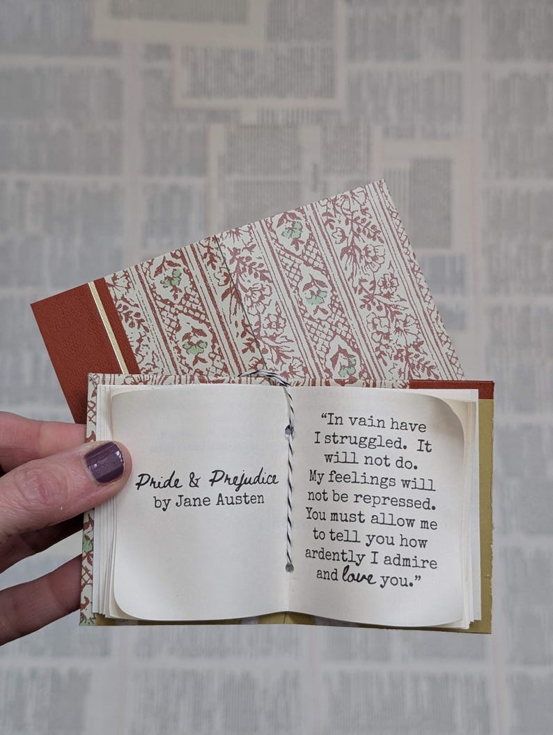 May include: A miniature book titled Pride & Prejudice by Jane Austen with a patterned cover. The open pages display the text: In vain have I struggled. It will not do. My feelings will not be repressed. You must allow me to tell you how ardently I admire and love you.