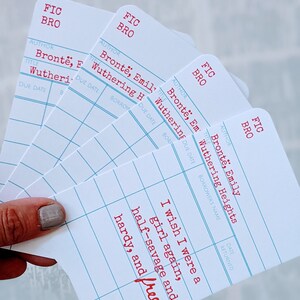 Puede incluir: Cuatro tarjetas blancas de estilo tarjeta de biblioteca con texto rojo. Las tarjetas est&aacute;n apiladas unas sobre otras. La tarjeta superior tiene el texto "Ojal&aacute; fuera una ni&ntilde;a otra vez, mitad salvaje y fuerte, y libre."