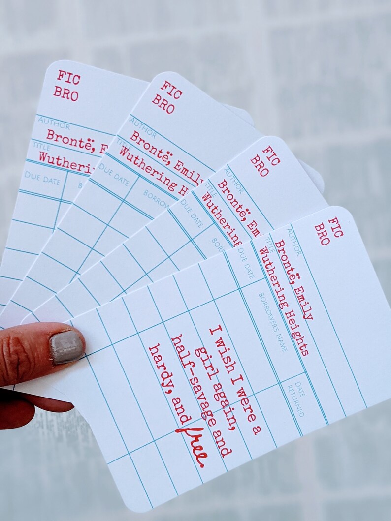 Puede incluir: Cuatro tarjetas blancas de estilo tarjeta de biblioteca con texto rojo. Las tarjetas est&aacute;n apiladas unas sobre otras. La tarjeta superior tiene el texto "Ojal&aacute; fuera una ni&ntilde;a otra vez, mitad salvaje y fuerte, y libre."