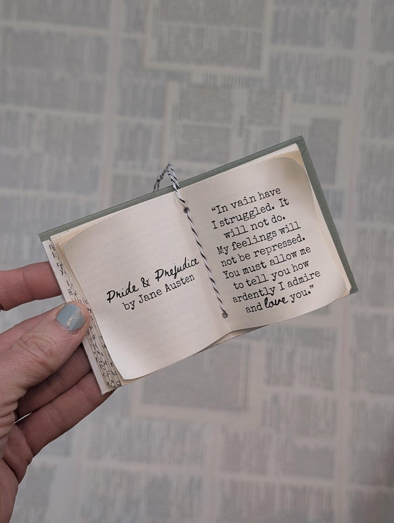 May include: A miniature book titled Pride & Prejudice by Jane Austen, featuring a black and white string binding. The open page displays the text: In vain have I struggled. It will not do. My feelings will not be repressed. You must allow me to tell you how ardently I admire and love you.