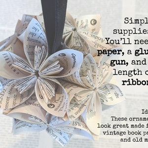May include: A close-up of a paper ornament made from book pages. The ornament is shaped like a flower and is hanging from a black ribbon. The text "Simple supplies! You'll need paper, a glue gun, and a length of ribbon!" is written in white text on a white background. The text "Ideas: These ornaments look great made from vintage book pages and old maps!" is written in black text on a white background.
