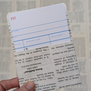 May include: A white library card with blue lines. The card has the word "FIC" in red at the top. The card has fields for "Author", "Title", "Due Date", "Borrower's Name", and "Date Returned".