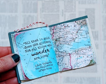May include: A small, blue and white book with a quote from J.R.R. Tolkien's The Fellowship of the Ring: "All that is gold does not glitter, Not all those who wander are lost." The book is open and a map is visible on the right page.