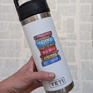 May include: White Yeti brand stainless steel water bottle with a sticker of a stack of books with titles like "Harry Potter", "The Secret Garden", "The Hobbit", and "Anne of Green Gables".