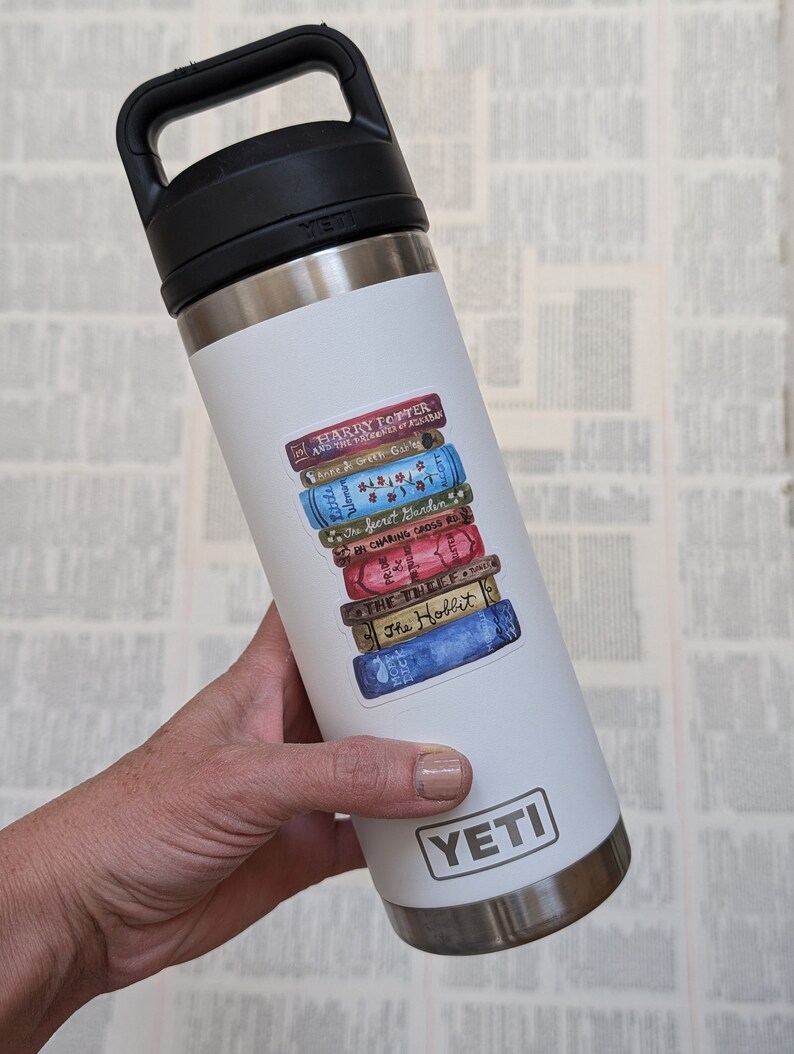 May include: White Yeti brand stainless steel water bottle with a sticker of a stack of books with titles like "Harry Potter", "The Secret Garden", "The Hobbit", and "Anne of Green Gables".