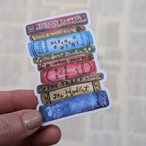 May include: A stack of colorful book stickers with titles like "Harry Potter and the Prisoner of Azkaban", "Anne of Green Gables", "Little Women", "The Secret Garden", "84 Charing Cross Road", "Pride & Prejudice", "The Thief", "The Hobbit", and "Moby Dick".
