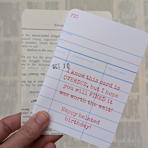 May include: A white library card with blue lines and red text that reads "I know this card is OVERDUE, but I hope you will FINED it was worth the wait! Happy belated birthday!"