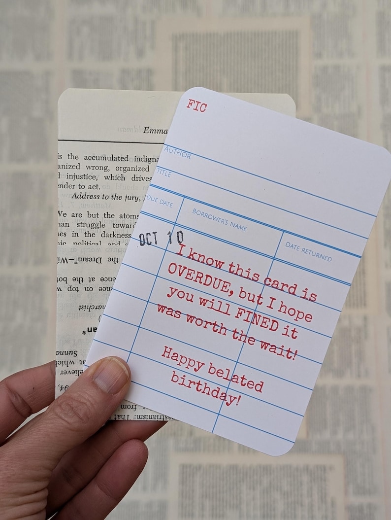 May include: A white library card with blue lines and red text that reads "I know this card is OVERDUE, but I hope you will FINED it was worth the wait! Happy belated birthday!"