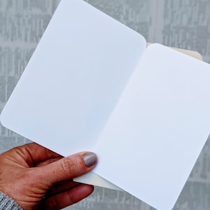 May include: A blank white card folded in half. The card is held in a hand with a light grey sweater sleeve visible.