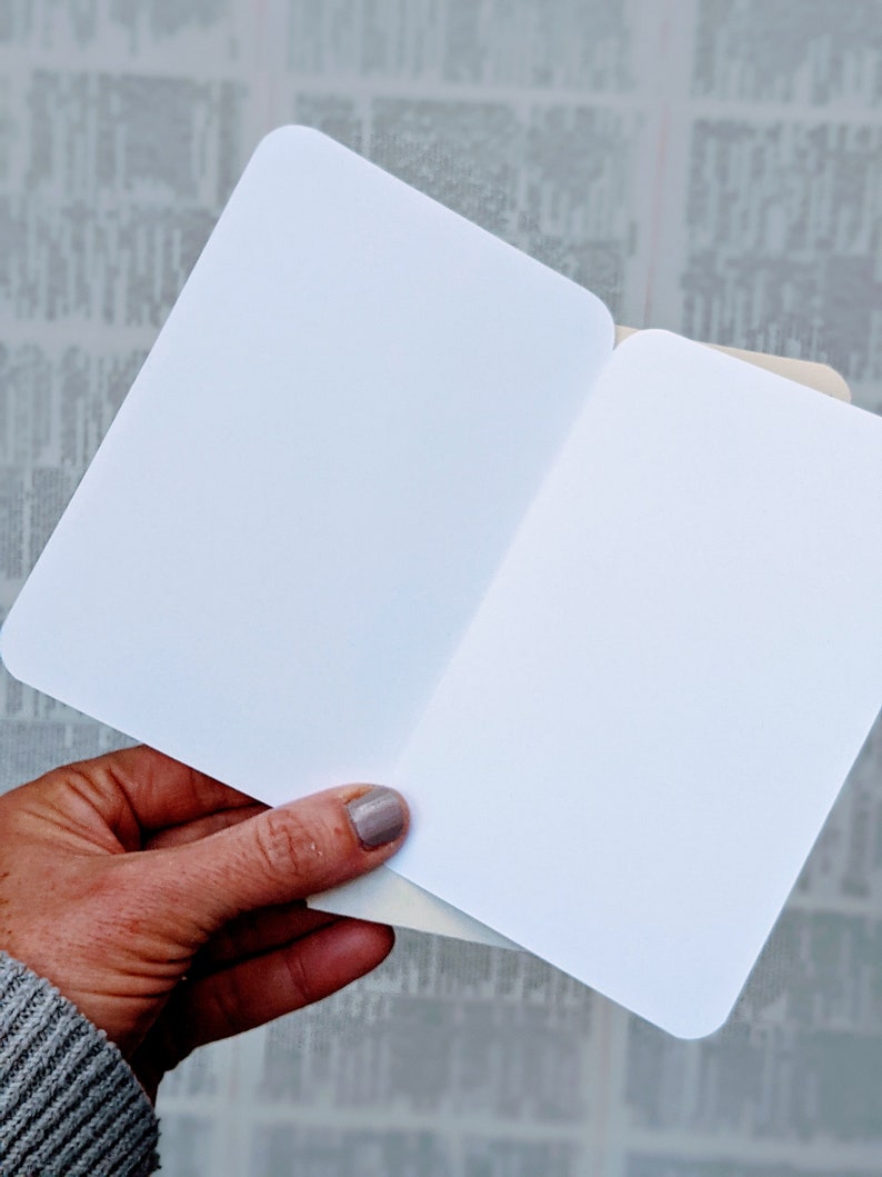 May include: A blank white card folded in half. The card is held in a hand with a light grey sweater sleeve visible.