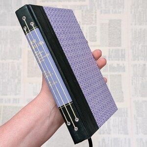 May include: A purple and black hardcover book with the title "Best Sellers" and a gold design on the spine. The book is held in a hand.