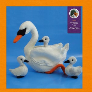 May include: A white felt swan with a black beak and orange accents, accompanied by three white felt cygnets. The swan has a long, curved neck and is surrounded by its young ones. The background is a solid blue.