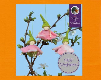 Op de afbeelding: Drie vilten poppen die aan een tak hangen met roze jurken en groene hoeden. De poppen zijn gelabeld "Vrolijke Vilt Vriendjes" en "PDF Pattern".
