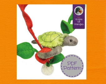 Op de afbeelding: Een vilt schildpad knutselpatroon, met een groene schild en grijs lichaam, wordt getoond op een rode stengel met groene bladeren. Het patroon is getiteld "Vrolijke Vilt Vriendjes" en bevat een PDF-patroon.