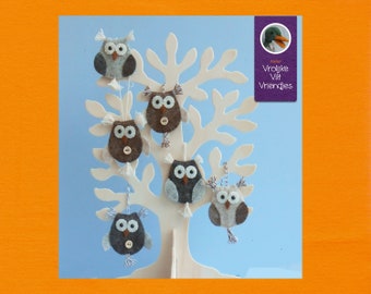 Op de afbeelding: Zes vilt uilen hangen aan een witte tak. De uilen zijn grijs, bruin en wit met zwarte ogen en bruine knopen. De uilen hangen aan een witte tak. De tak bevindt zich op een blauwe achtergrond. De tekst "Atelier Vrolijke Vilt Vriendjes" staat op een paarse rechthoek in de rechterbovenhoek van de afbeelding.